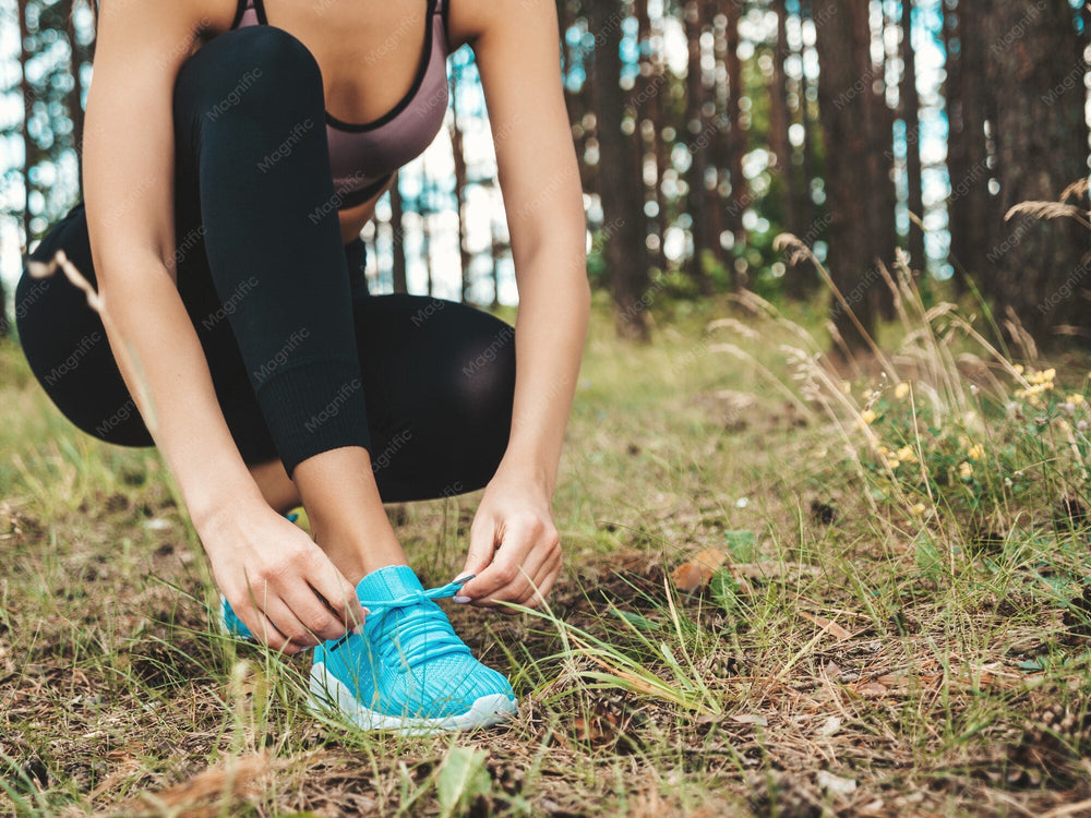 Sportlerin bindet vor dem Lauftraining im Wald ihre Schuhe
